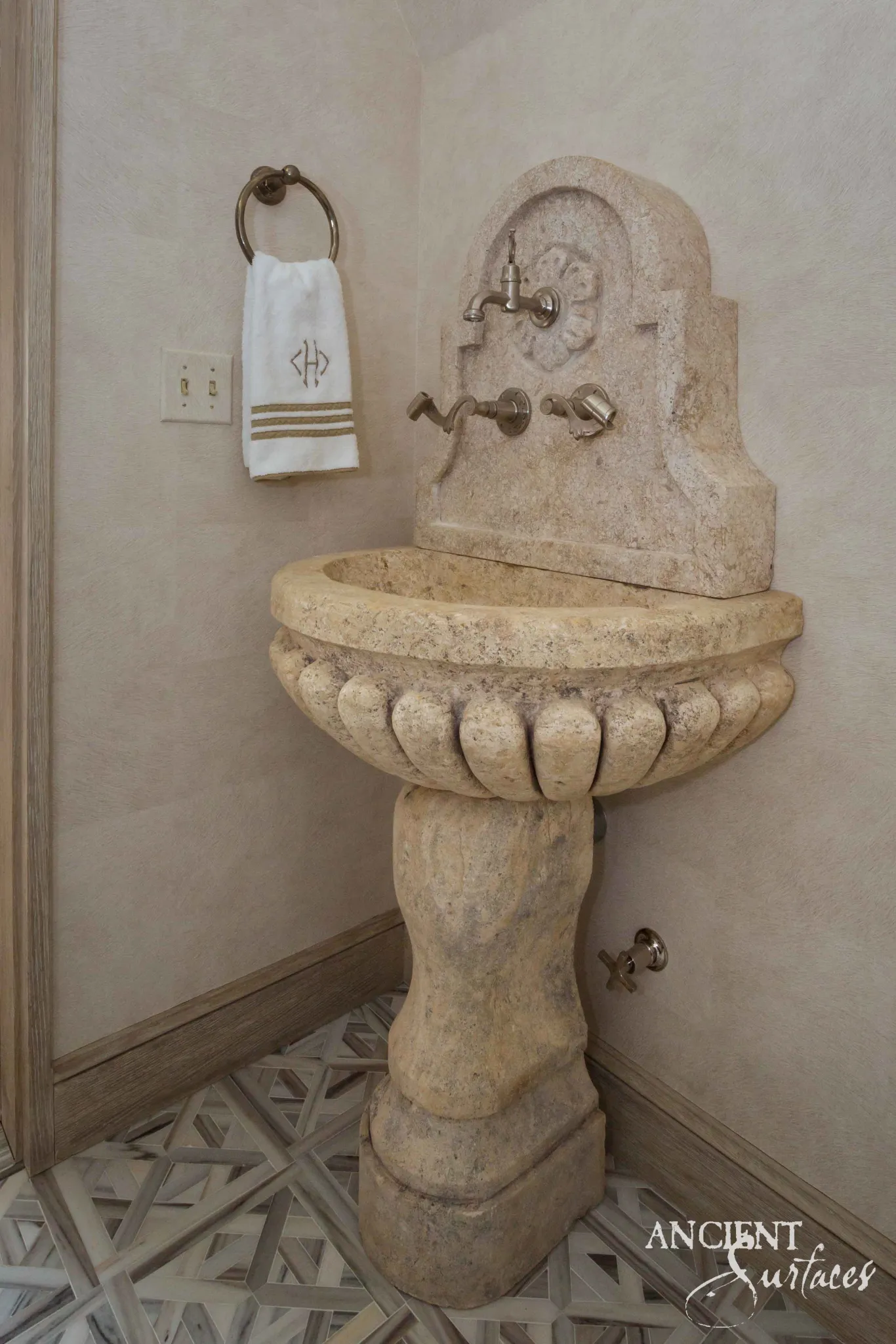 Reclaimed antique limestone pedestal sink from Ancient Surfaces with a scalloped gadrooned basin and an arched carved backplate, fitted into the corner of a bathroom
