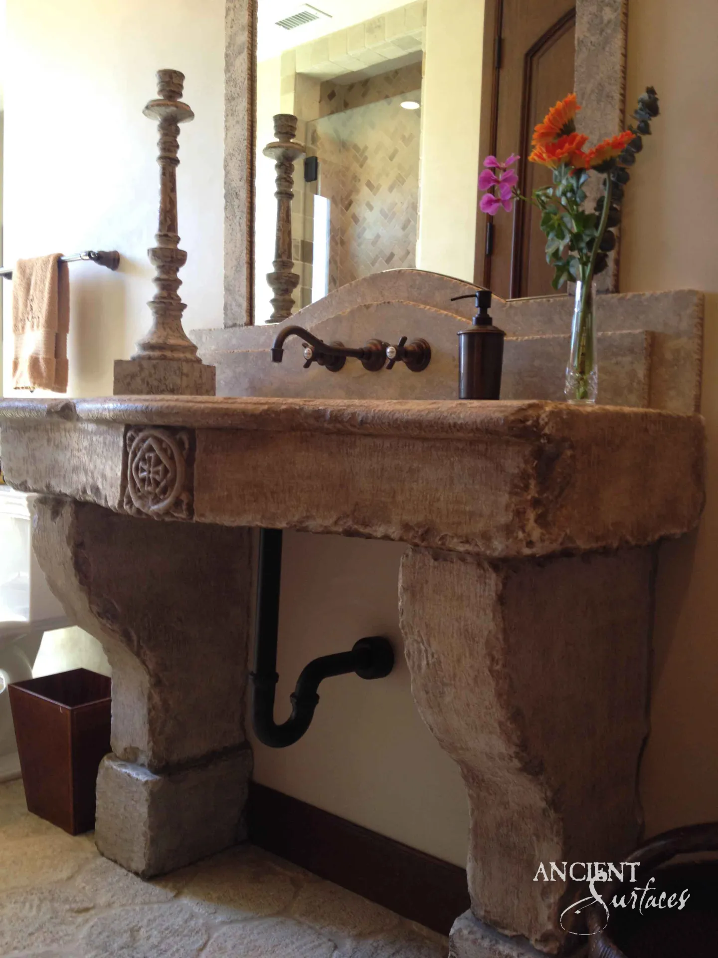 Reclaimed antique limestone console sink from Ancient Surfaces carved with a roundel medallion, resting on two scrolled corbel legs beneath a large mirror