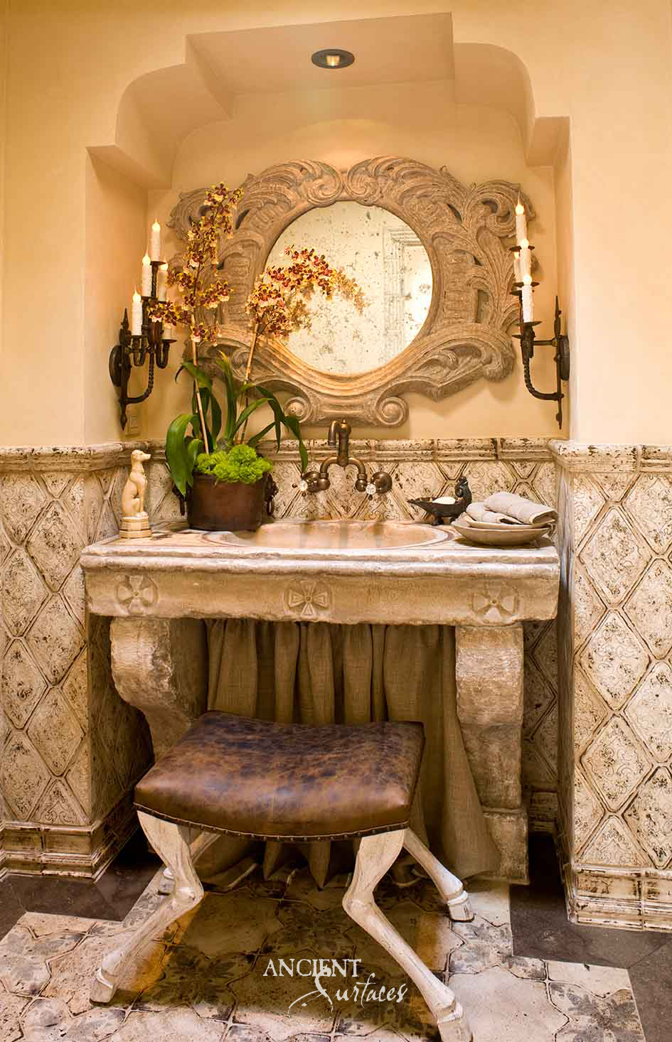 Reclaimed antique carved limestone console sink from Ancient Surfaces with roundel medallions on its apron, set beneath a matching carved stone mirror in a candlelit powder room
