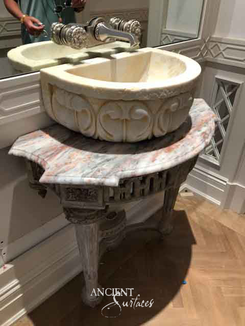Reclaimed antique carved stone vessel bowl from Ancient Surfaces with a quatrefoil and rosette pattern, set atop an ornate variegated stone console