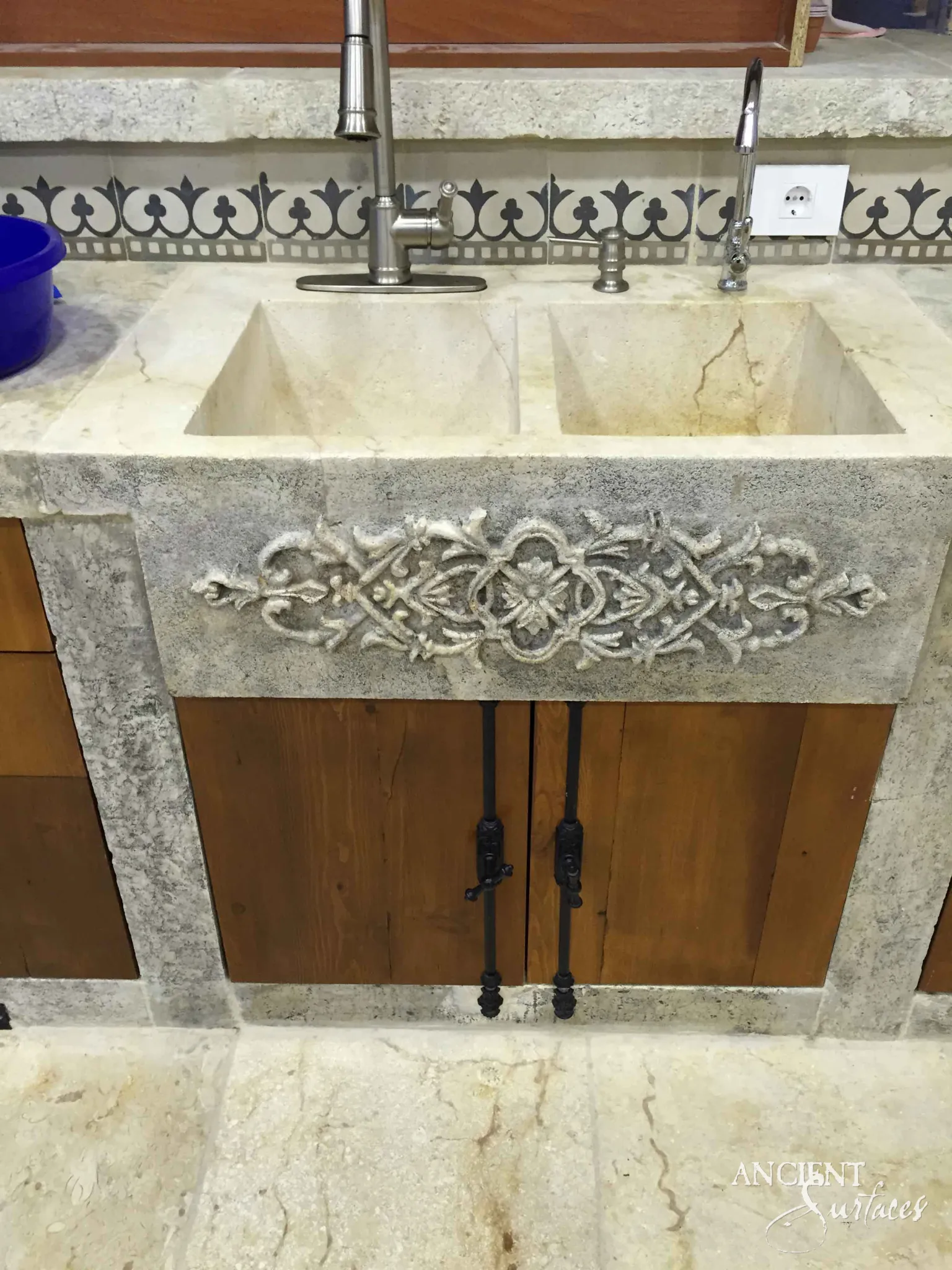 Reclaimed antique limestone double basin trough sink from Ancient Surfaces with a carved foliate apron, set into a farmhouse kitchen island with wood cabinetry