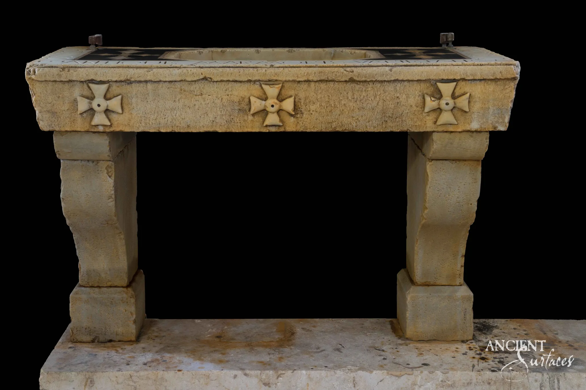 Reclaimed antique limestone console sink from Ancient Surfaces with three carved cross medallions on its apron and a dark inset stone top, photographed against black