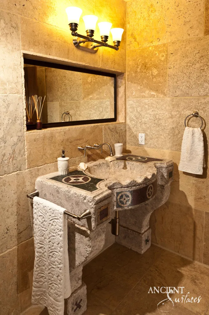 Reclaimed antique limestone trough vanity sink from Ancient Surfaces with a black and white star mosaic inlaid top and a carved foliate apron, installed in a stone lined bathroom